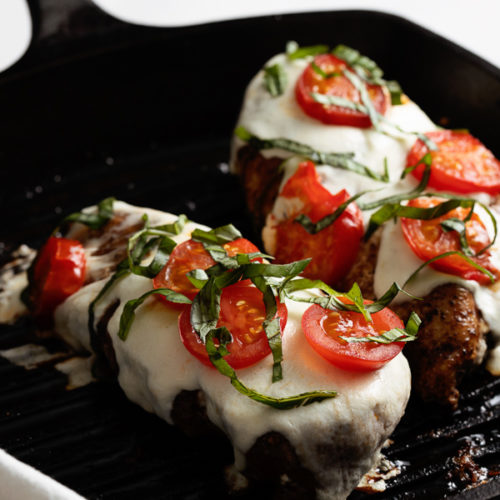 Cast Iron Grill Pan with two finished grilled chicken caprese chicken breasts sitting atop a white background.