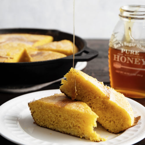 sliced cornbread on white plate with drizzled honey