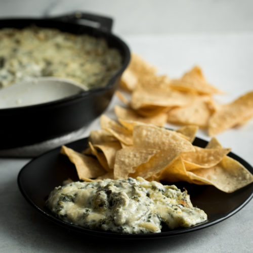 Spinach and artichoke dip in a cast iron skillet with chips on a black plate