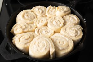 adding the cinnamon rolls to the cast iron skillet to cook