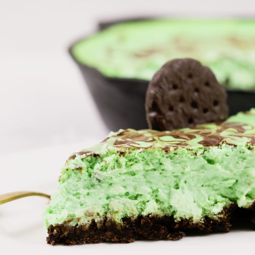 slice of thin mint cheesecake on white plate with thin mint cookie on top