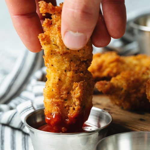 hand dipping chicken tenders into sauce