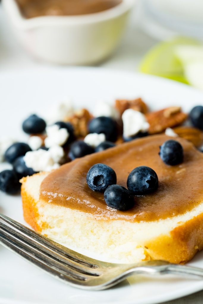 A close up image of apple butter spread on a piece of pound cake and topped with blueberries. Pound cake is on a simple white plate with an antique fork.