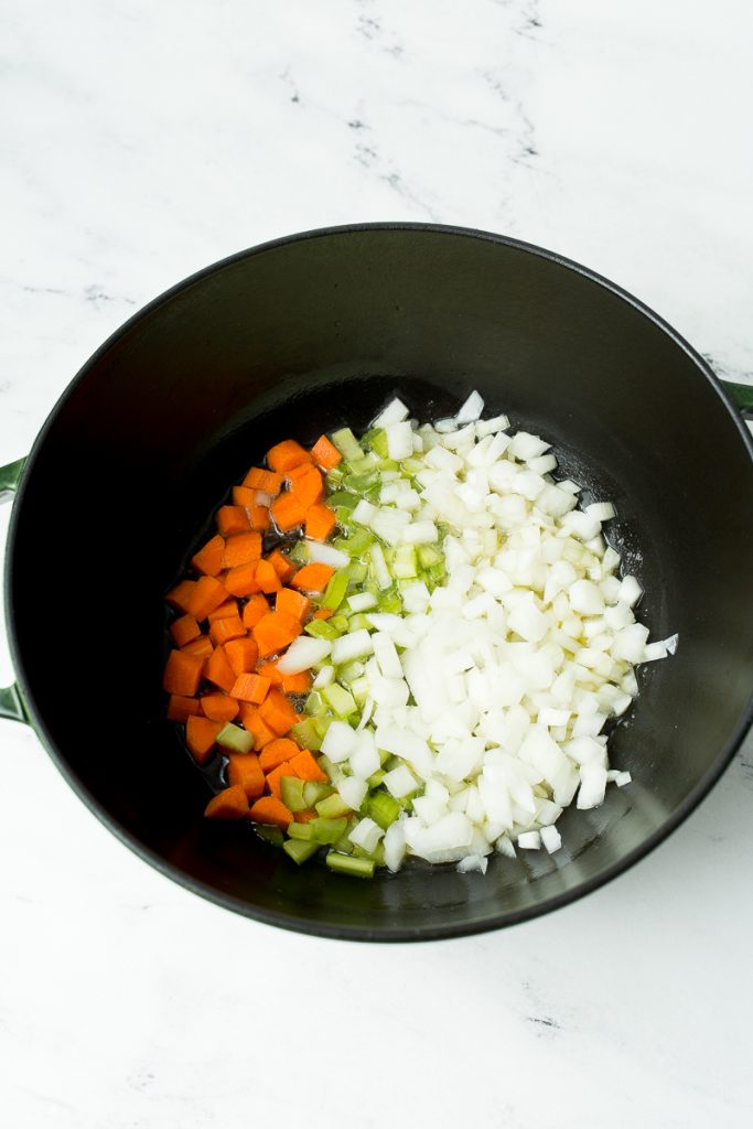 Diced carrots, celery, and onions saute in a large cast iron dutch oven.