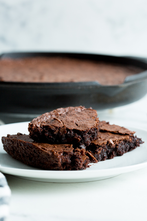 Close up image of three cast iron skillet brownies stacked on a white plate with the cast iron skillet in the background.