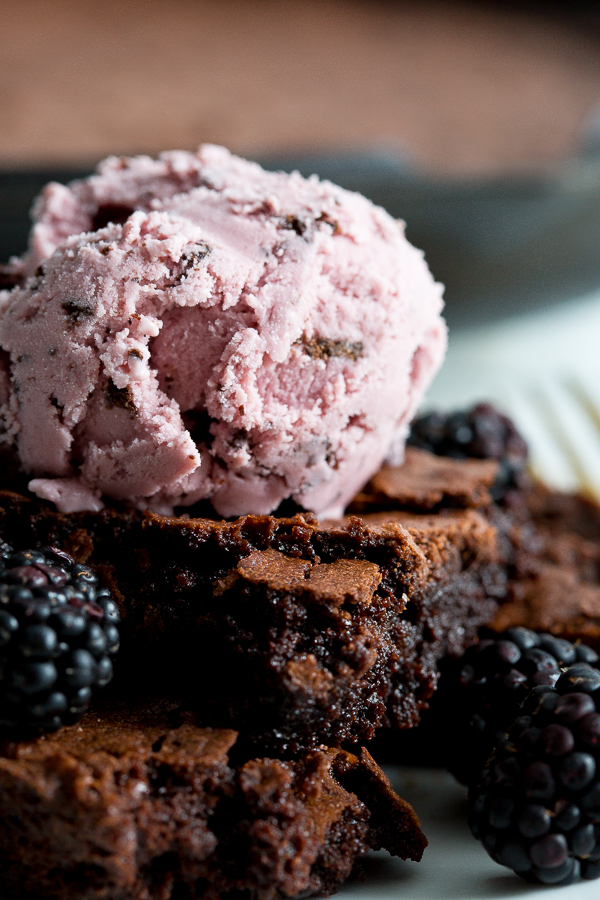 Close up image of homemade fudge brownies surrounded by blackberries and topped with a scoop of black raspberry ice cream.