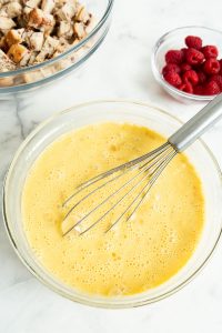 An image of the egg and eggnog mixture required for eggnog french toast casserole. With cinnamon bread and raspberries in the background.