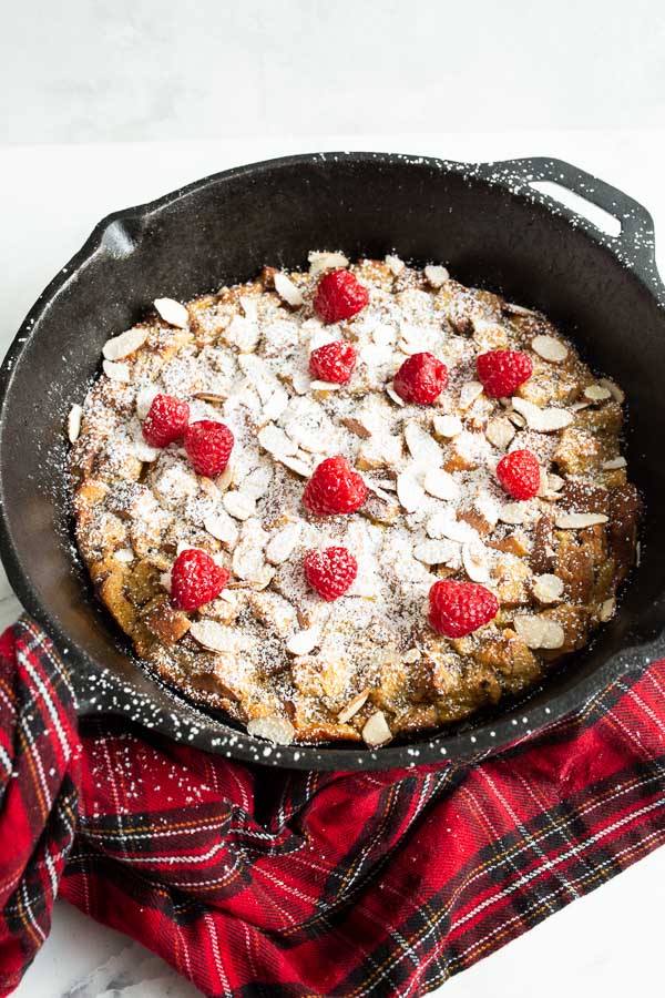 Eggnog french toast casserole in a cast iron 12 inch skillet dusted with powdered sugar and dotted with fresh raspberries