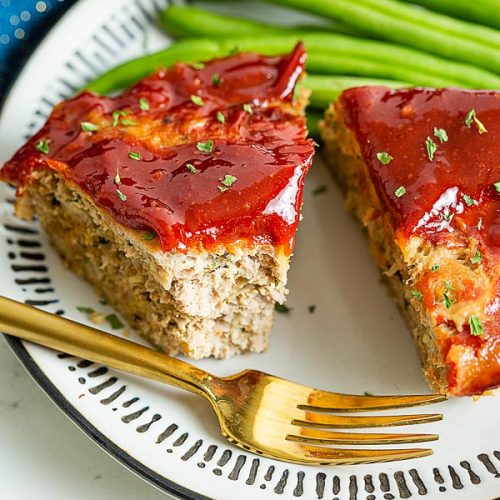 A close up of ground turkey meatloaf with spicy ketchup glaze and fresh green beans, missing one bite.