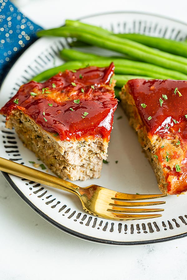 A close up of ground turkey meatloaf with spicy ketchup glaze and fresh green beans, missing one bite.