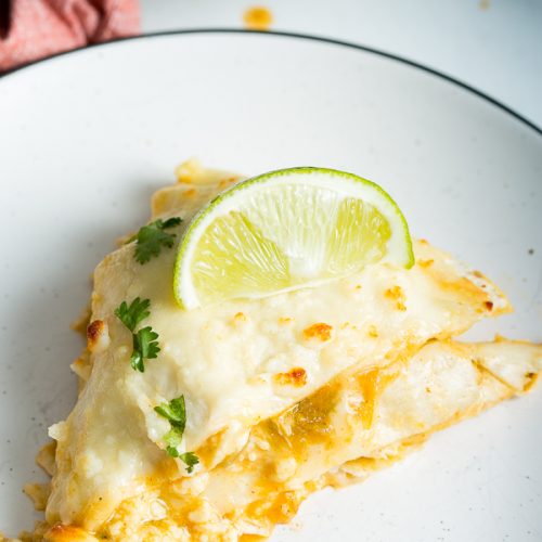 A 45* angle image of green enchilada lasagna on a plate topped with lime and cilantro.