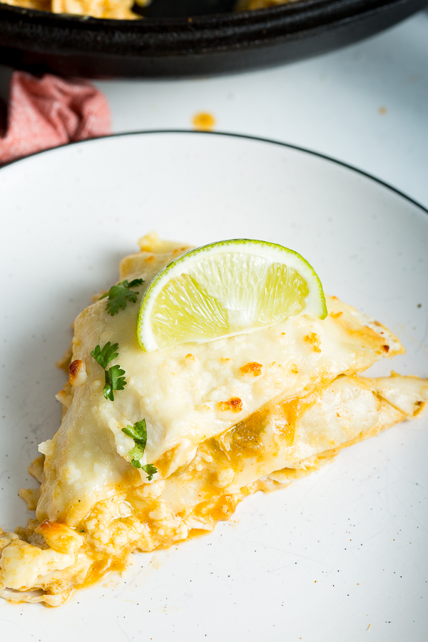 An overhead shot of Green Chicken Enchilada Lasagna topped with cilantro and a lime wedge on a white plate with a black rim.