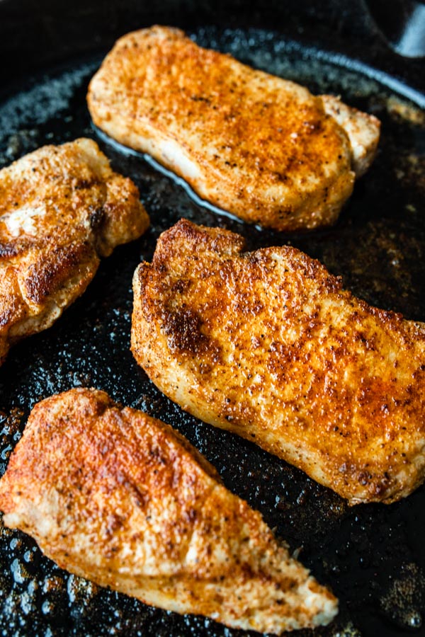 A close up image of pan seared pork chops on a cast iron skillet