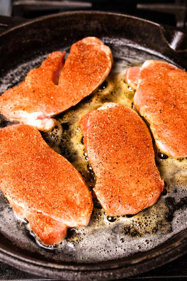 A side process shot of raw boneless pork chops being cooked in a cast iron skillet.
