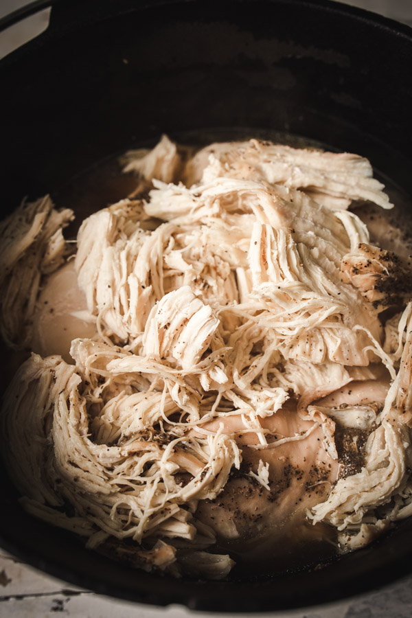 A cast iron dutch oven filled with over five pounds of shredded chicken.