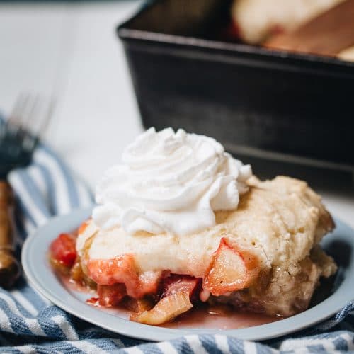 Side image of rhubarb cobbler on a plate with a cast iron baking dish in the background.