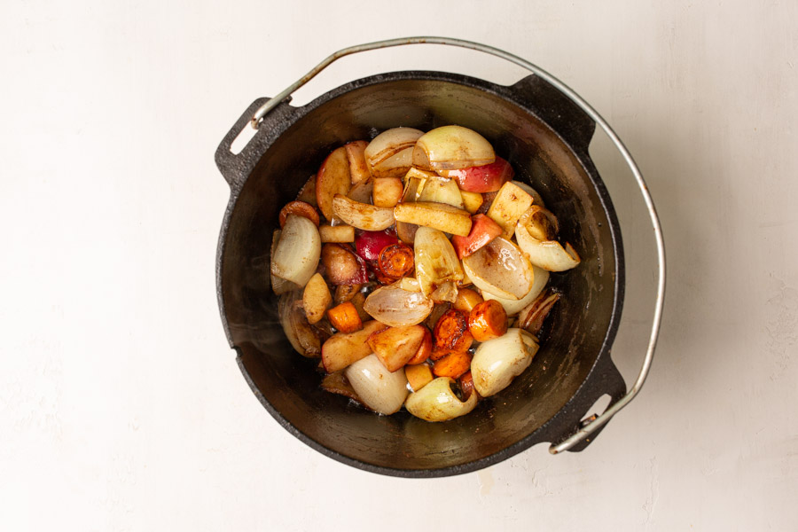 Overhead image of carrots, onions, apples, and spices in a dutch oven. 