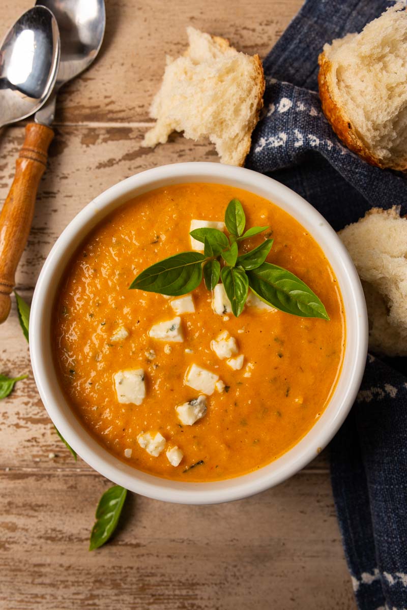 Overhead image of tomato basil soup in a white bowl topped with fresh basil and gorgonzola cheese. 