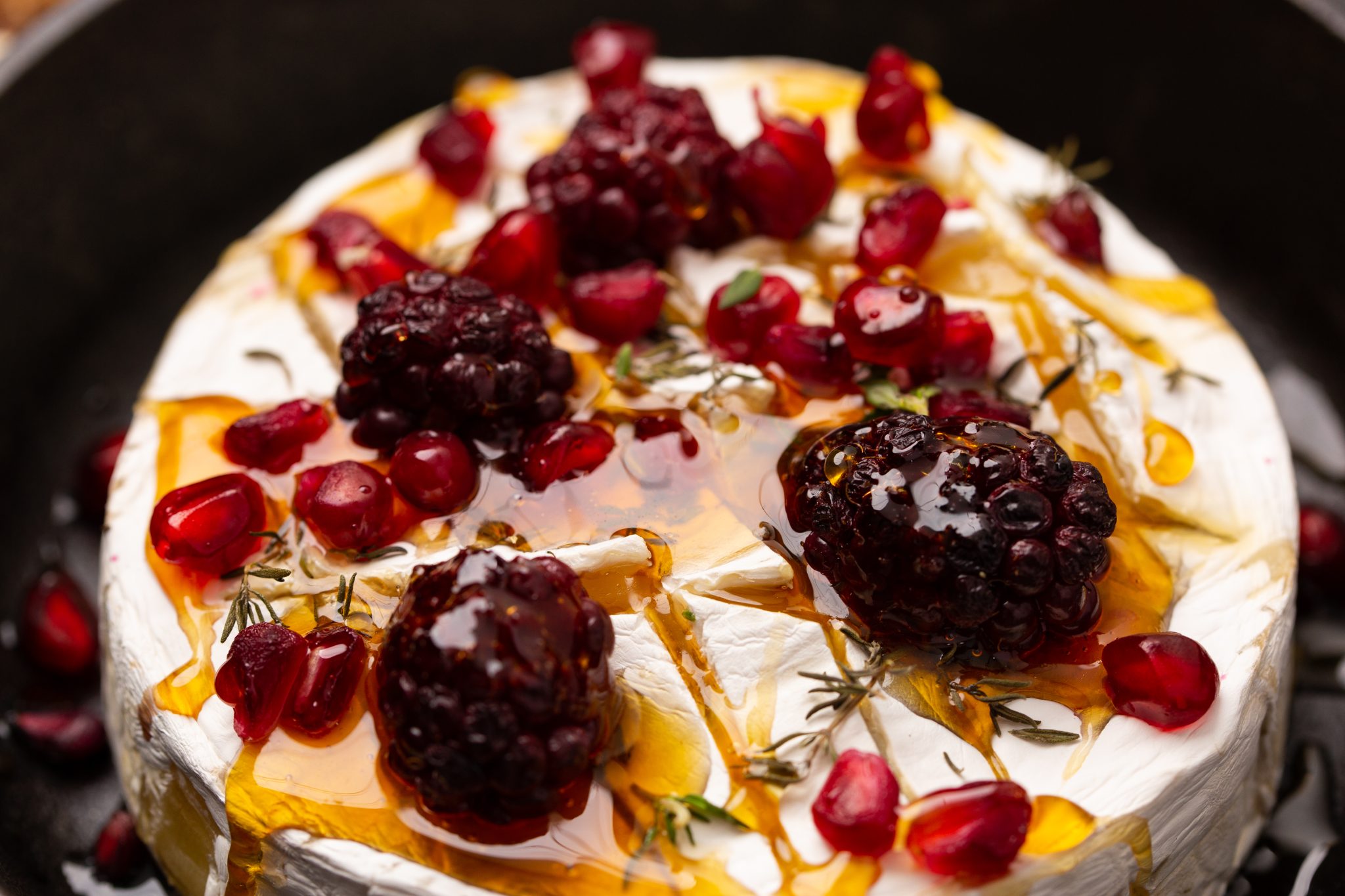 Close up image of baked brie drizzled with honey in a cast iron skillet