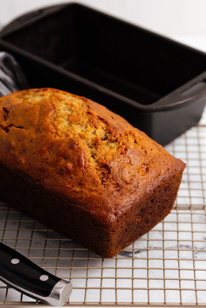 side image of banana nut bread cooling on a wire rack with a cast iron loaf pan in the back.