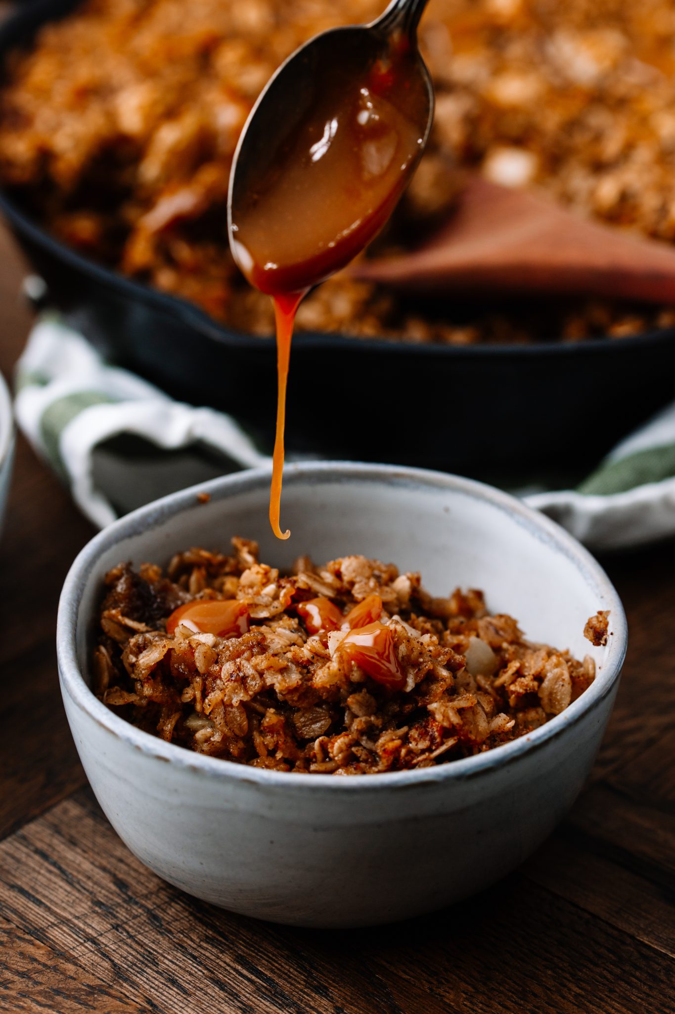 Caramel Apple Cinnamon Baked Oatmeal in a cast iron skillet with caramel sauce being drizzled on top. 