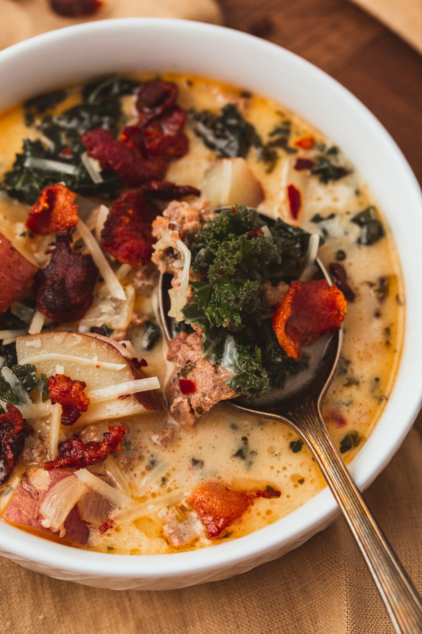 zuppa toscana in a bowl with a spoon topped with shredded parmesan cheese