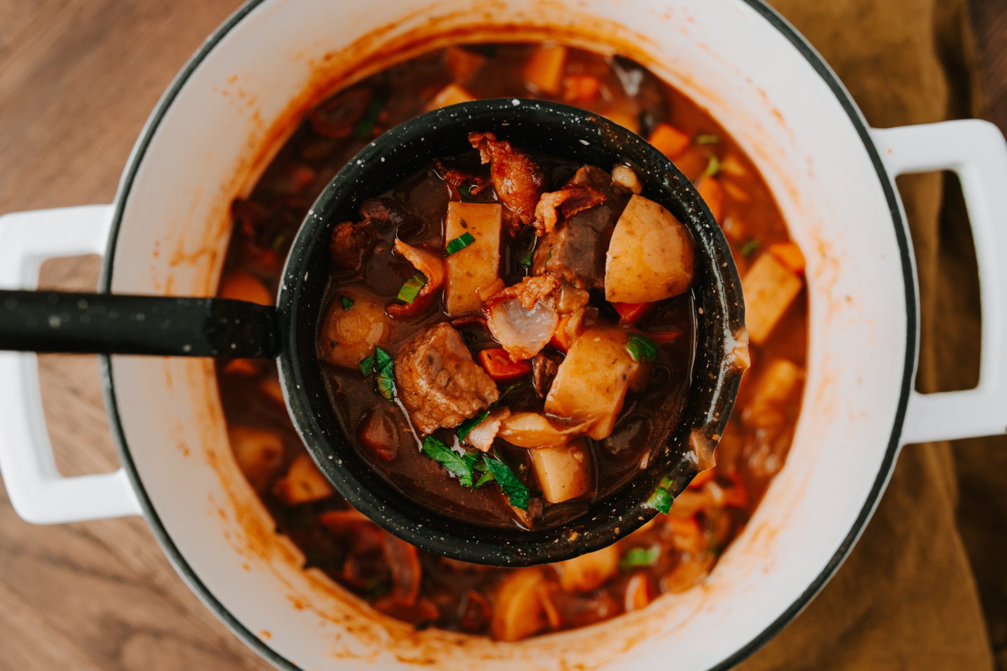 Overhead image of guinness beef stew in a dutch oven with a ladle scooping some out. 