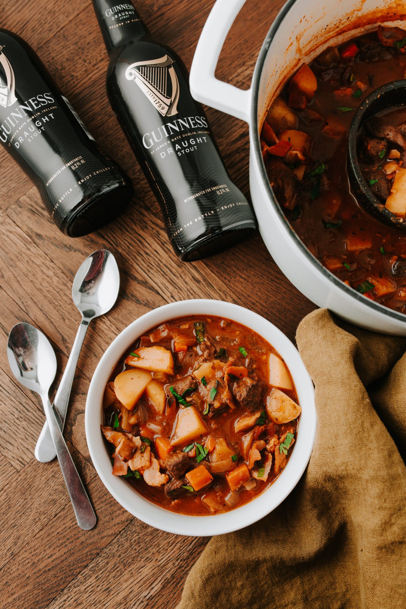 Overhead image of Guinness Beef Stew next to two bottles of guinness beer, a bowl and dutch oven of beef stew. 