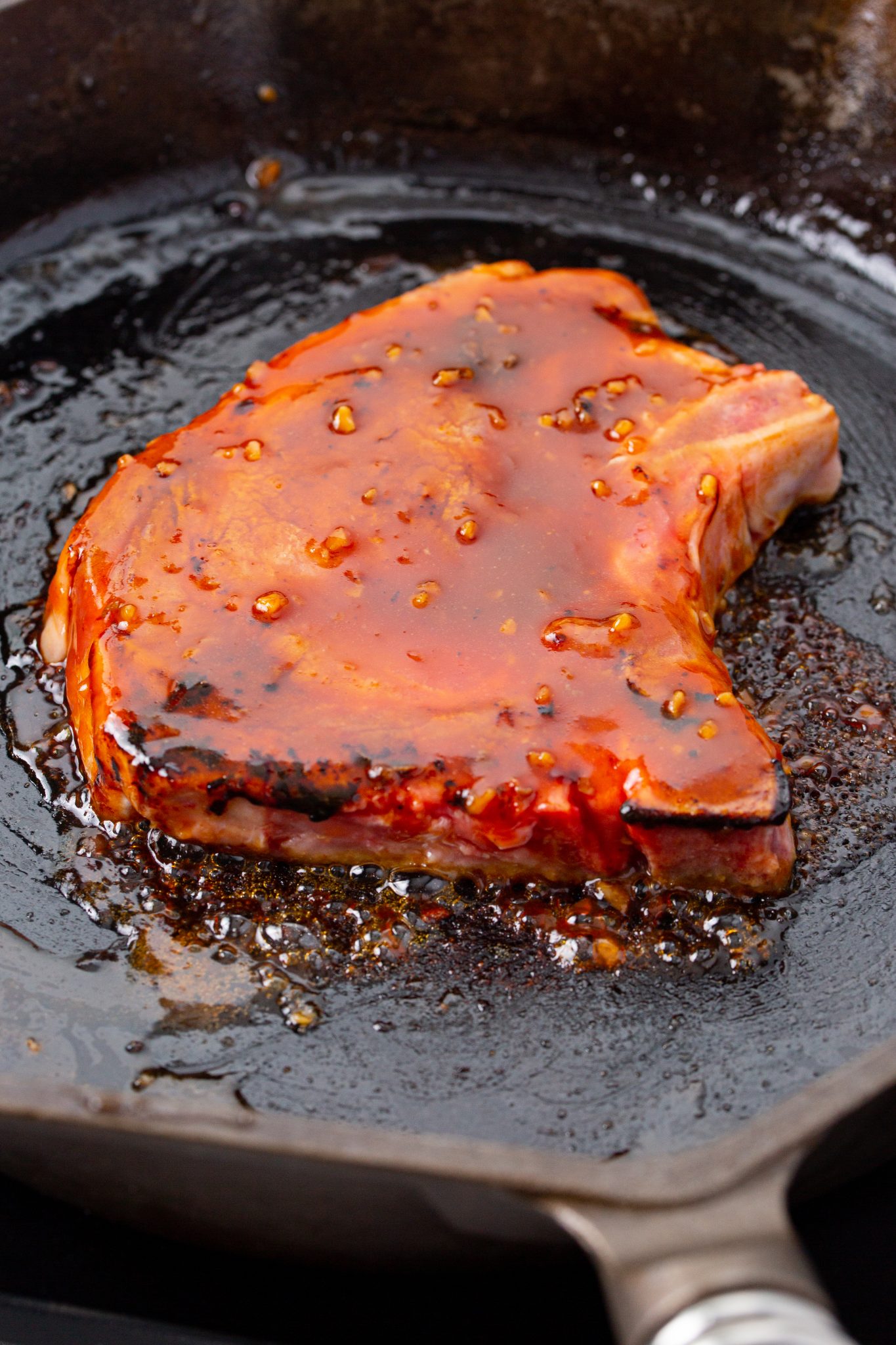Asian style bone in pork chops searing in a cast iron skillet