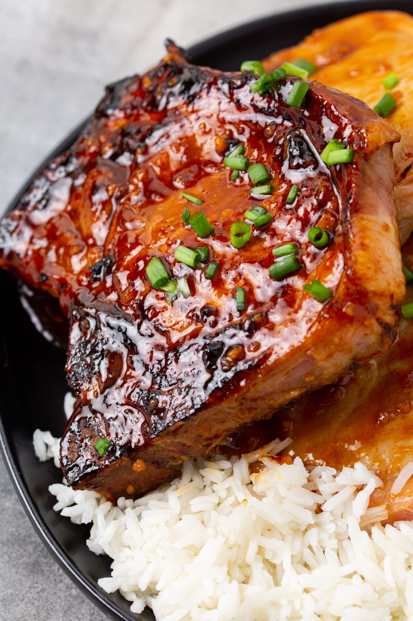 Asian Style Hoisin Glazed Bone In Pork Chops served with rice and garnished with chives