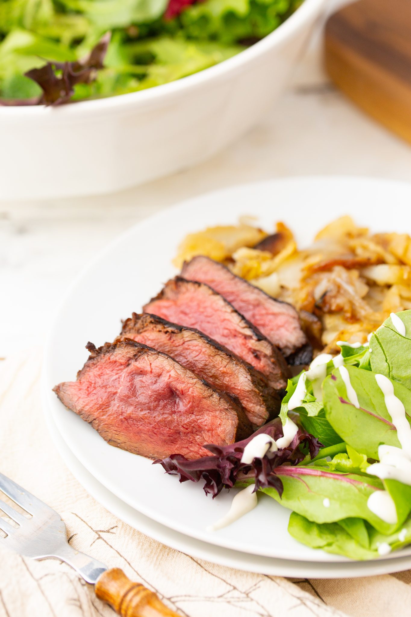 Grilled venison backstrap sliced into medallions served on a plate with potatoes and salad.