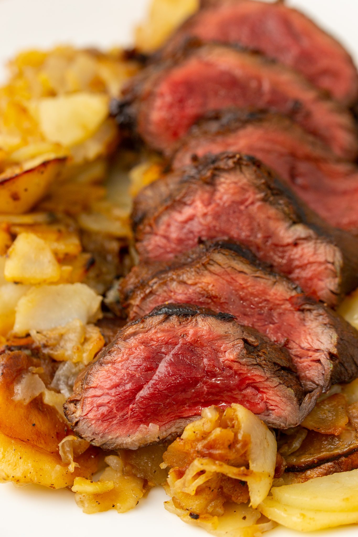 close up image of venison backstrap on a plate of sauted potatoes and onions
