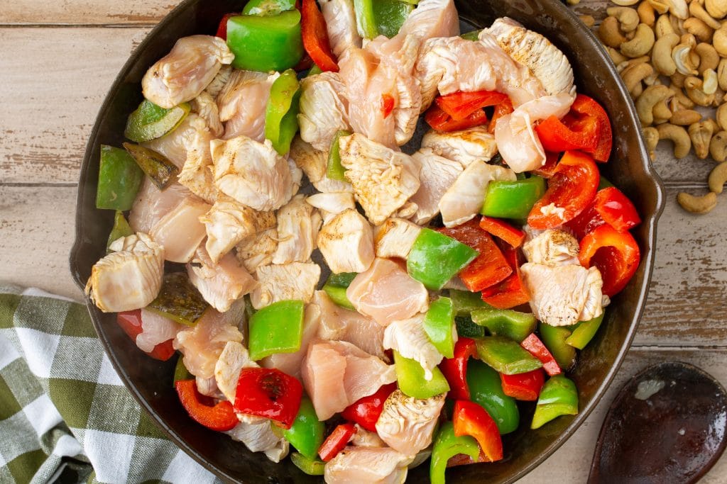 chicken and bell peppers being cooked in a cast iron skillet for cashew chicken