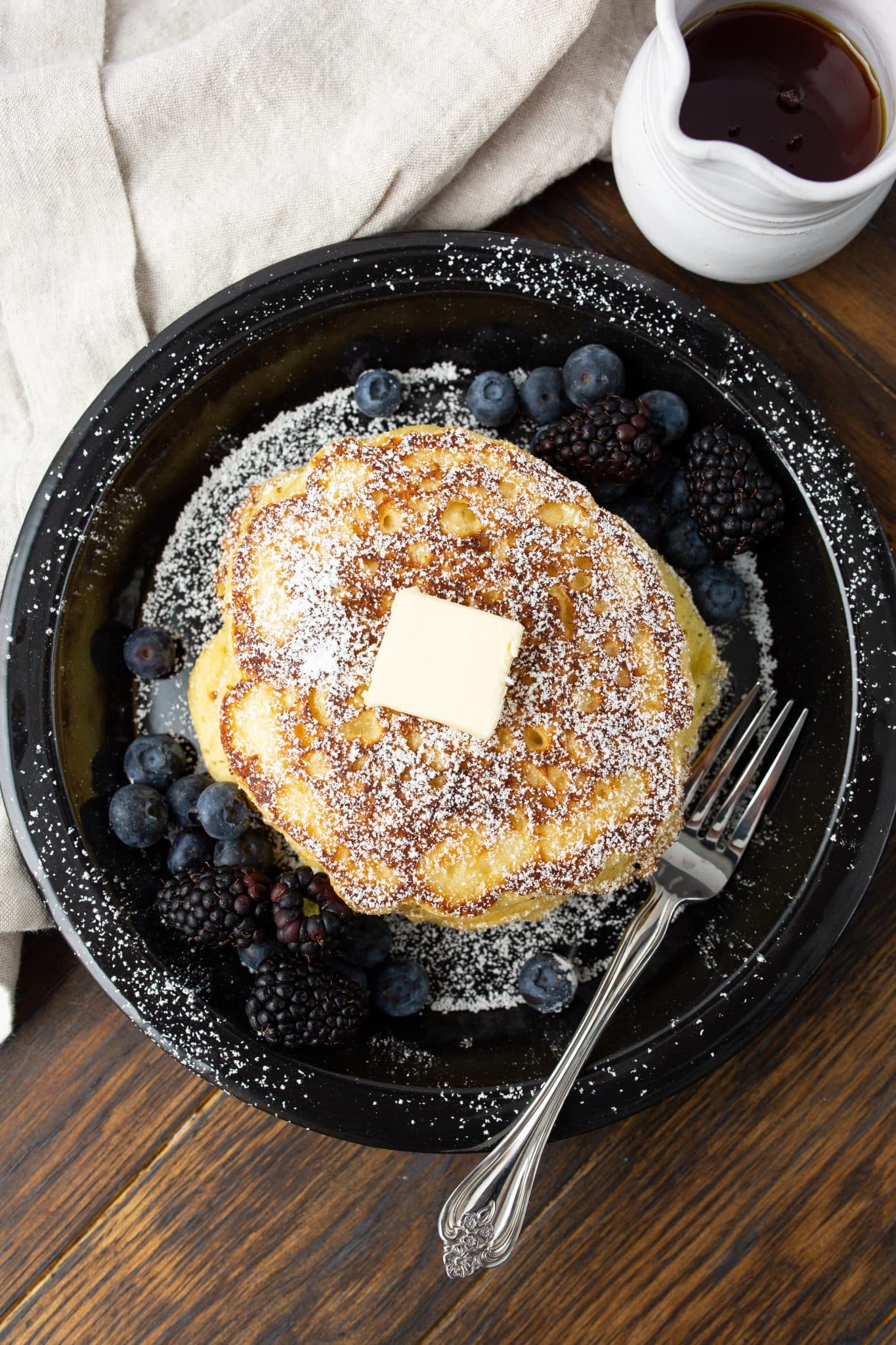 overhead image of buttermilk pancakes stacked on a plate surrounded by fresh berries