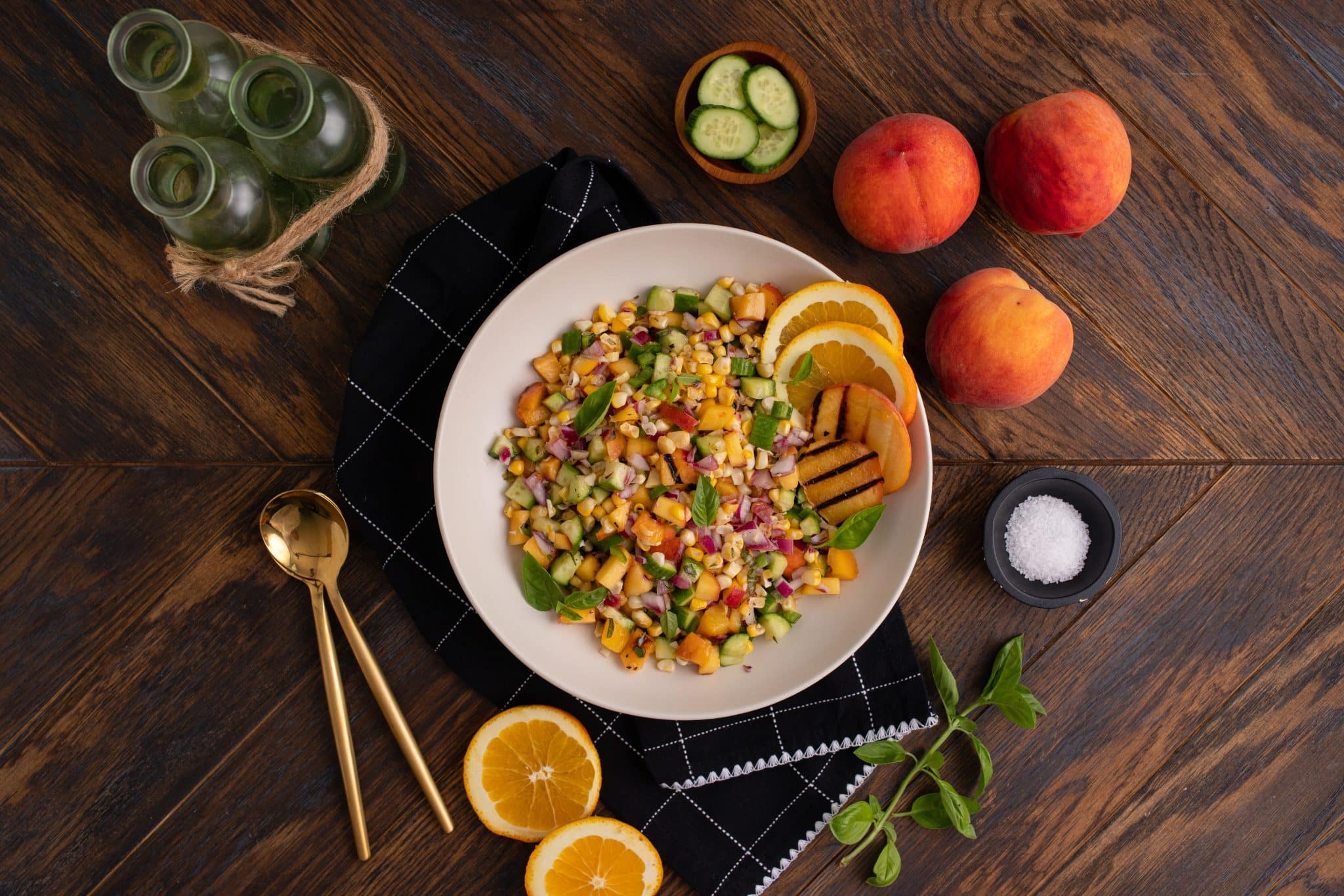 overhead image of corn cob salad on a table with basil, peaches, and orange