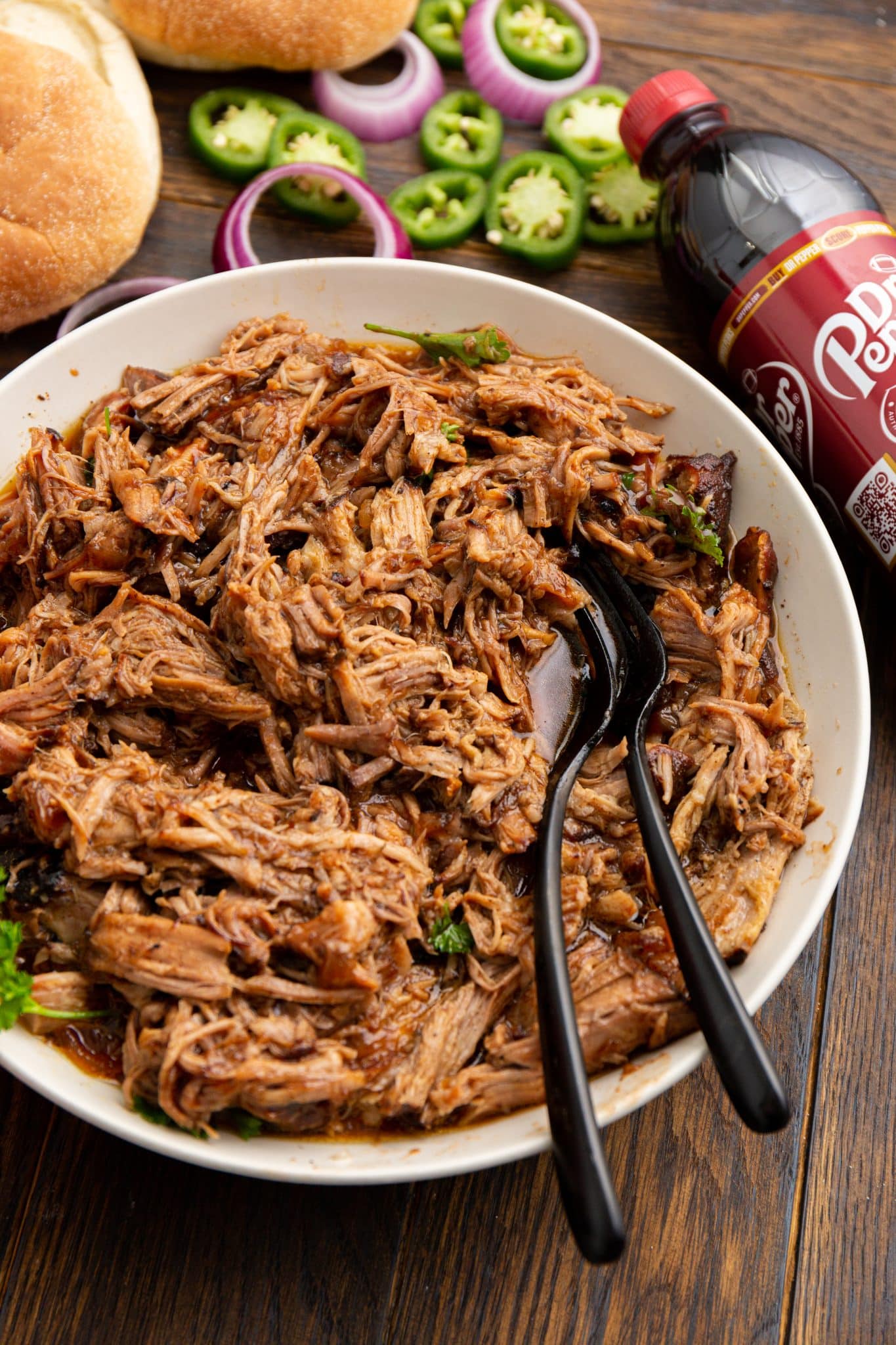 Shredded pulled pork in a bowl next to a bottle of Dr Pepper