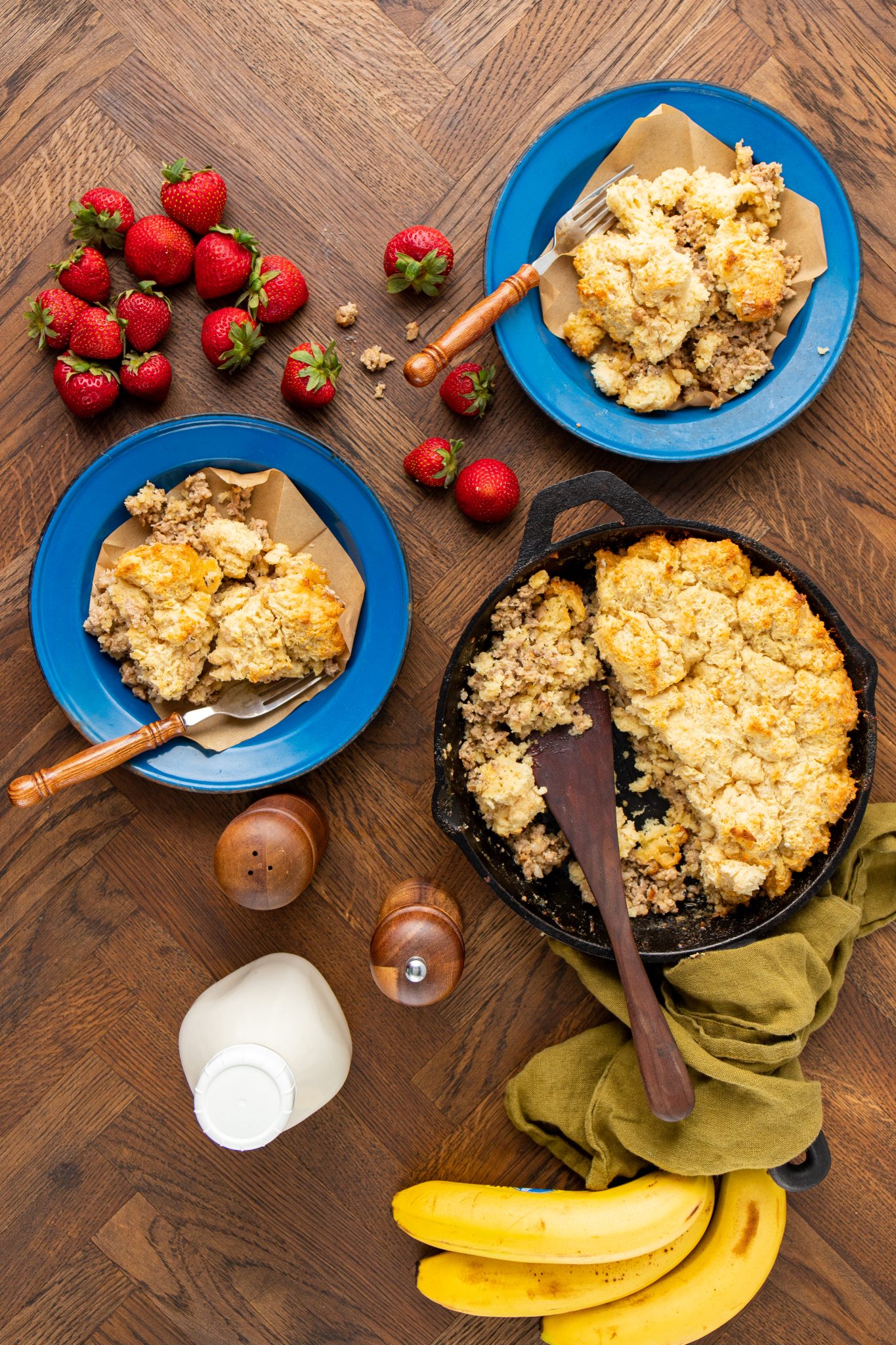 overhead image of sausage gravy and drop biscuit casserole in a cast iron skillet and camping plates
