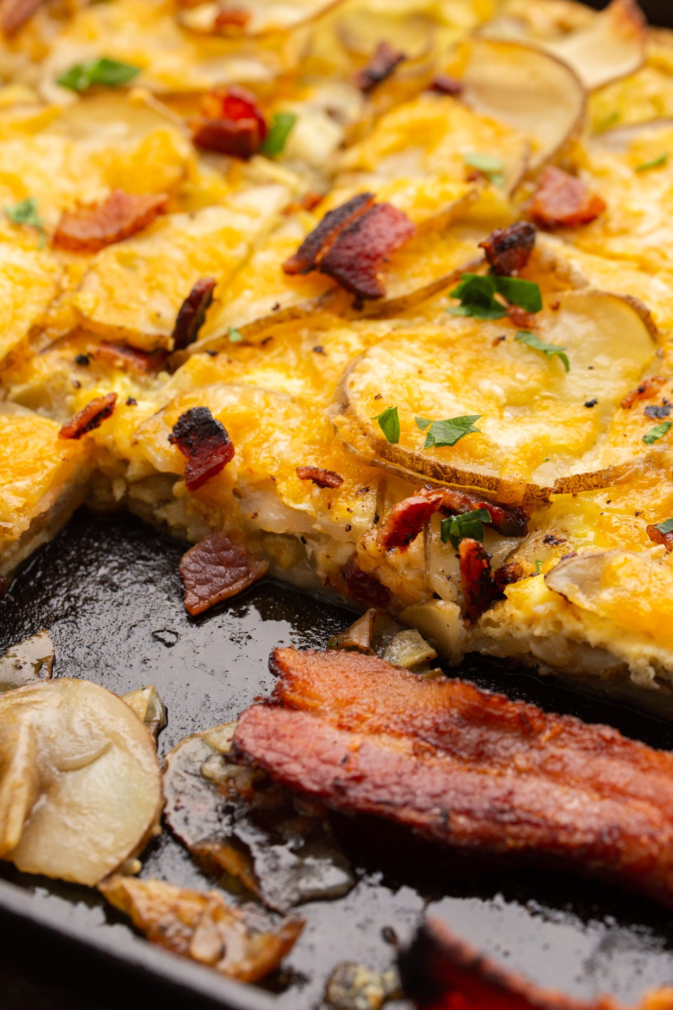close up of cheesy scalloped potato breakfast casserole topped with bacon