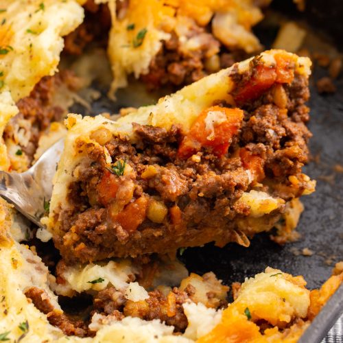 A close up image of cottage pie being served from a cast iron casserole dish