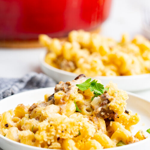 Philly cheesesteak mac and cheese served on a small white plate in front of a bright red dutch oven.