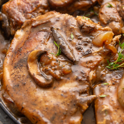 Salisbury Pork Chops with mushrooms, onions, thyme, and gravy in a cast iron skillet