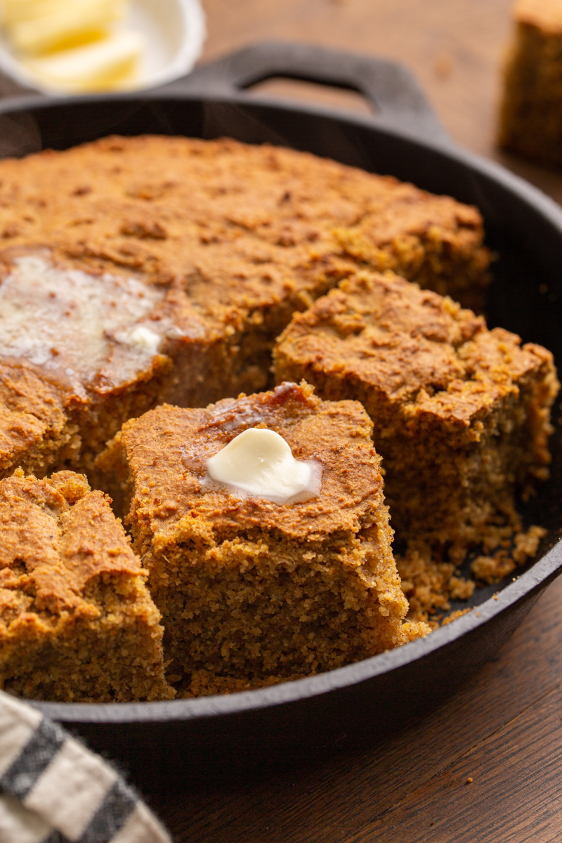golden brown sweet potato cornbread in a cast iron skillet topped with butter. 