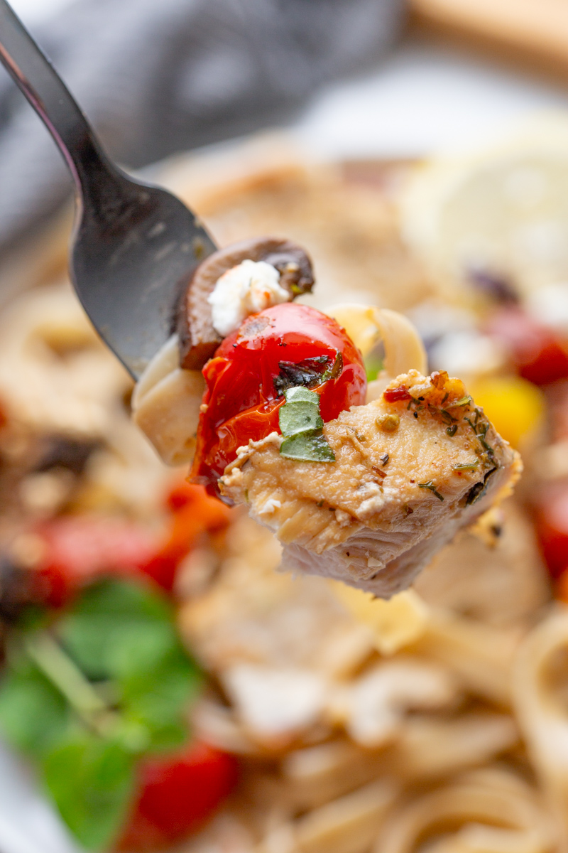 bite shot of greek chicken on a fork with olives, mushrooms, feta and tomato