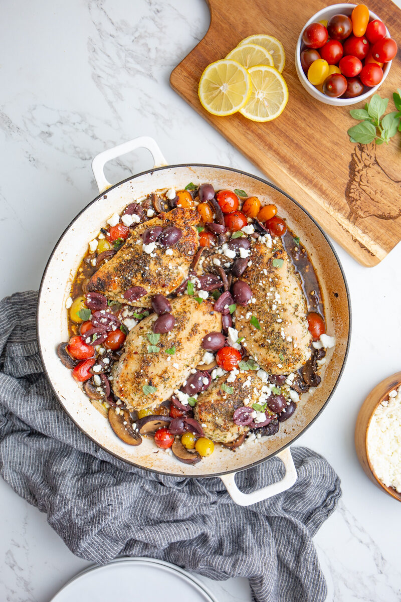 large skillet with chicken, tomatoes, mushrooms, and olives